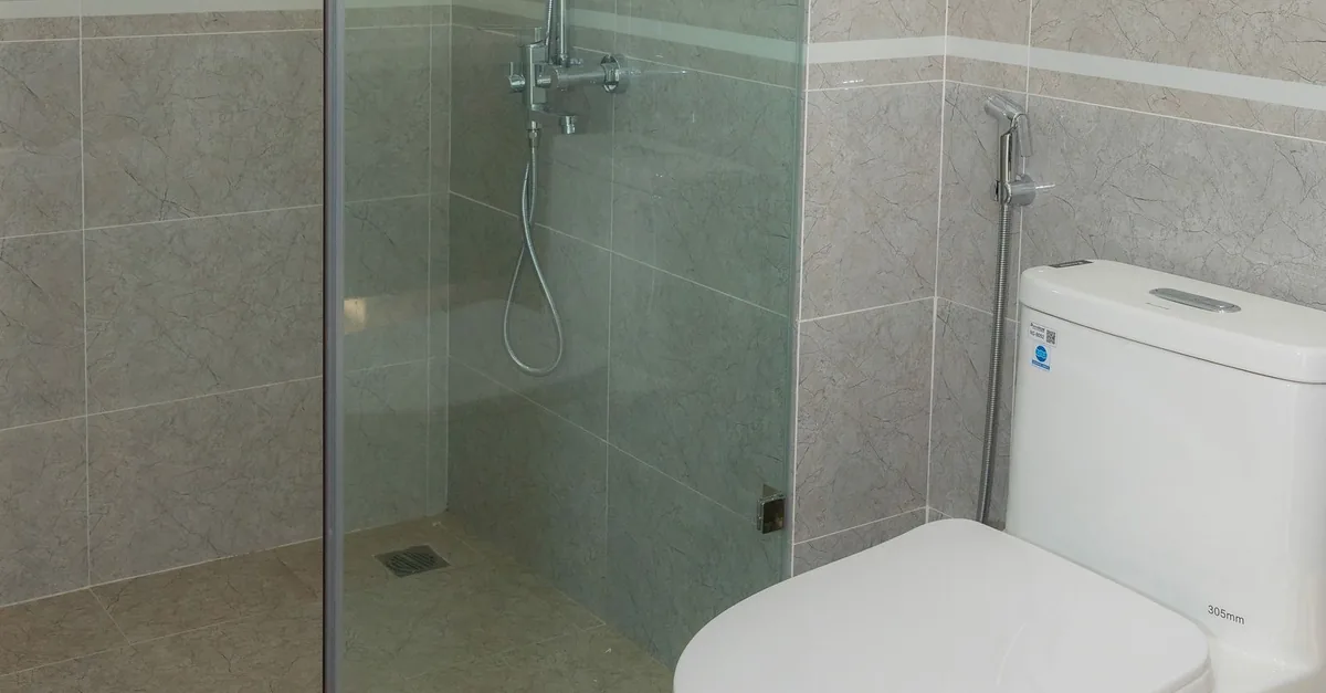 A glass shower enclosure and toilet side by side in a tiled bathroom